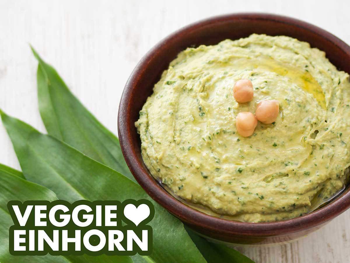 Bärlauch Hummus in einer Schale und frische Bärlauchblätter