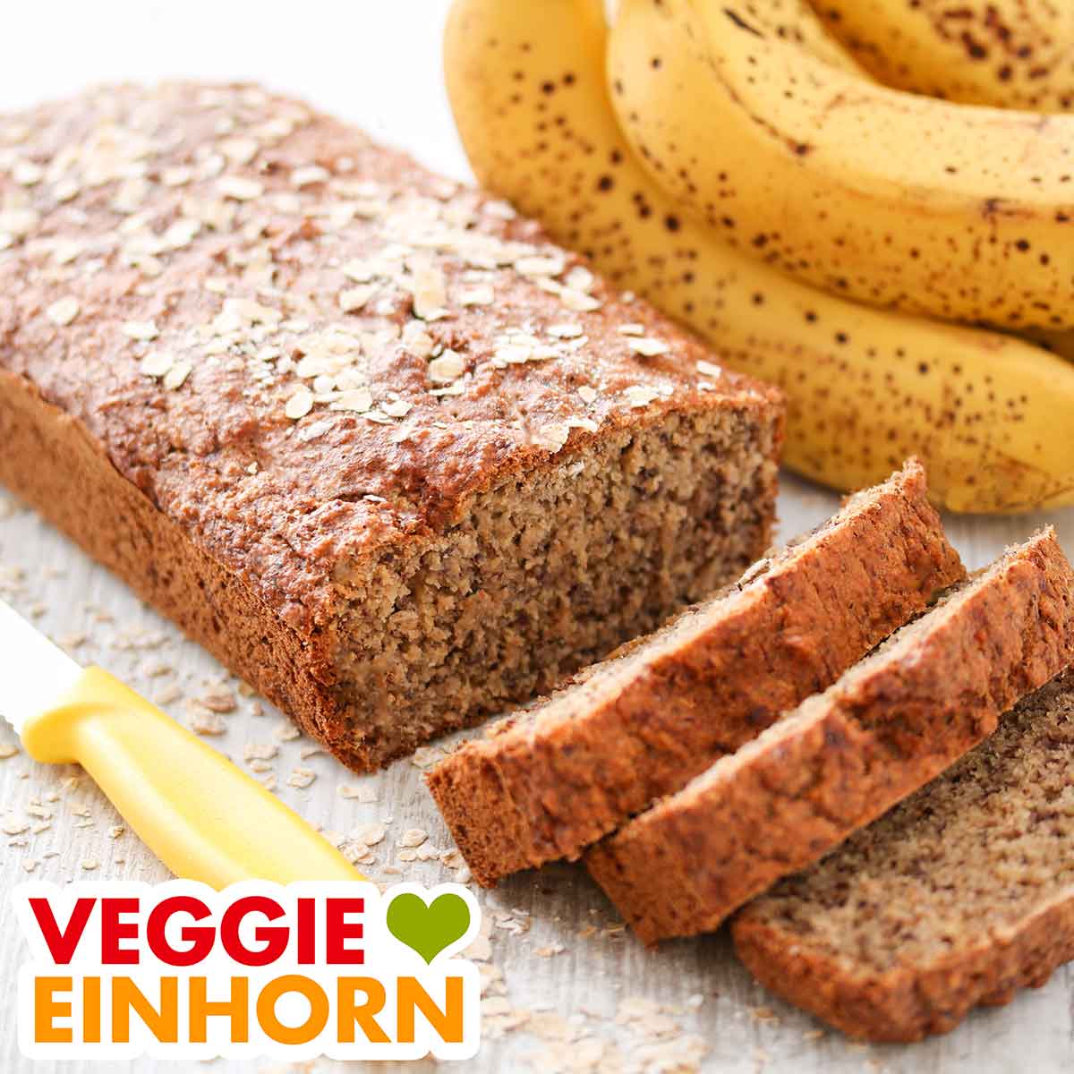 Ein angeschnittenes Bananenbrot mit Haferflocken und einigen reifen Bananen