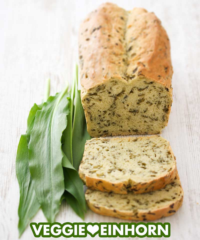 Ein angeschnittenes Bärlauchbrot und frische Bärlauchblätter