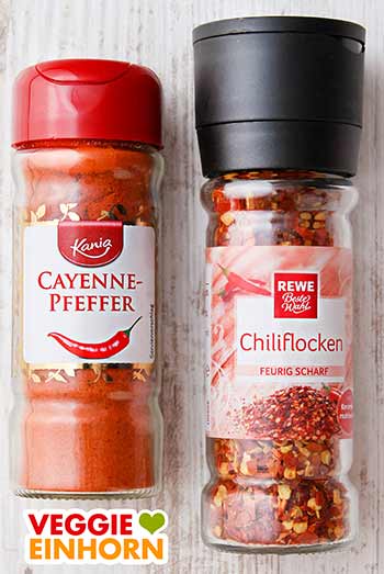 Cayennepfeffer oder Chiliflocken Ein Glas Cayennepfeffer und eine Gewürzmühle mit Chiliflocken