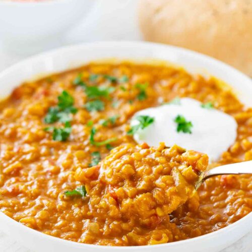 Nahaufnahme eines Tellers mit veganem roten Linsen-Dal, garniert mit frischer Petersilie und einem Klecks pflanzlichem Joghurt.