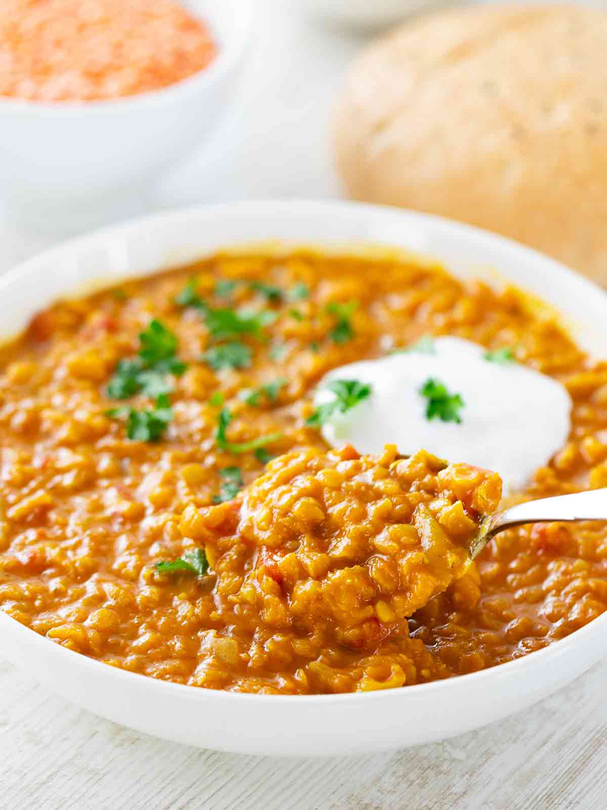 Nahaufnahme eines Tellers mit veganem roten Linsen-Dal, garniert mit frischer Petersilie und einem Klecks pflanzlichem Joghurt.