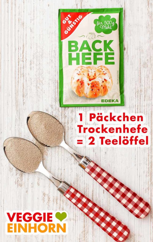Ein Päckchen Trockenhefe und zwei Teelöffel mit Trockenhefe auf einem Tisch