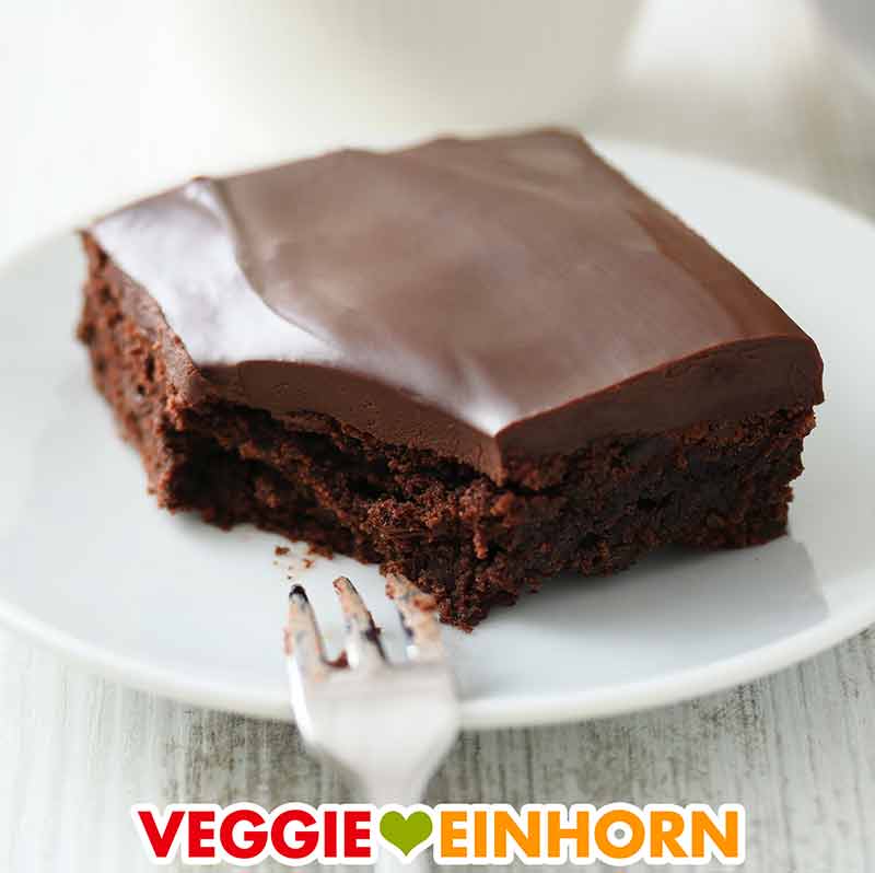 Veganer Brownie mit Schokoüberzug Ein veganer Brownie mit cremiger Schokoglasur auf einem Teller