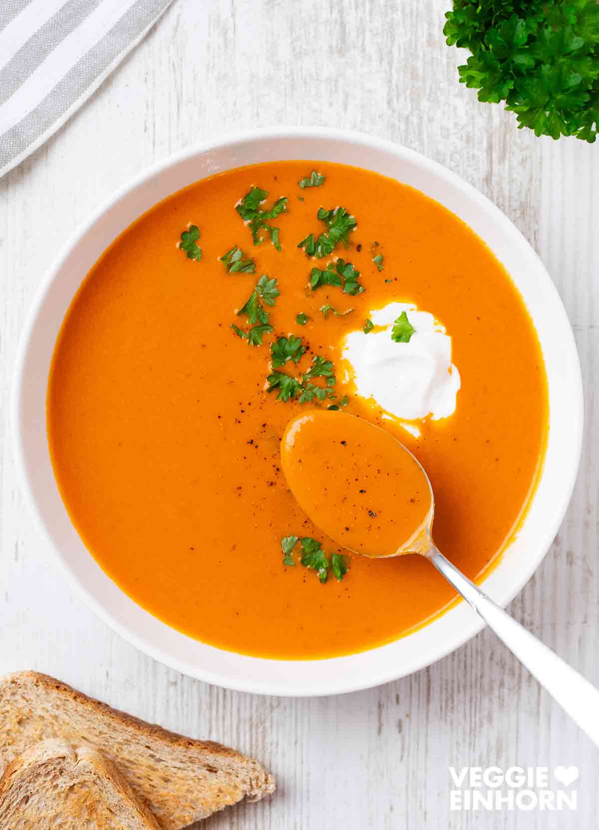Tomatensuppe mit Kokosmilch und frischer Petersilie auf einem Teller mit einem Löffel.