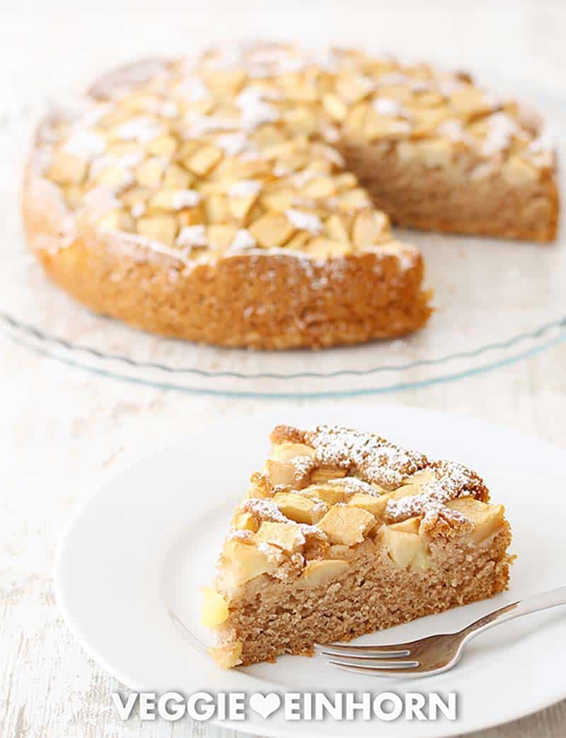 Veganer Apfelkuchen auf einer Kuchenplatte und ein Stück Kuchen auf einem Teller