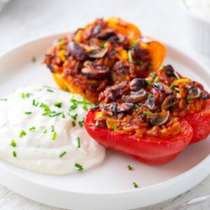 Vegane gefüllte Paprika mit einer herzhaften Mischung aus Reis, Kidneybohnen, Mais und Champignons, serviert auf einem weißen Teller mit veganem Kräuterquark.