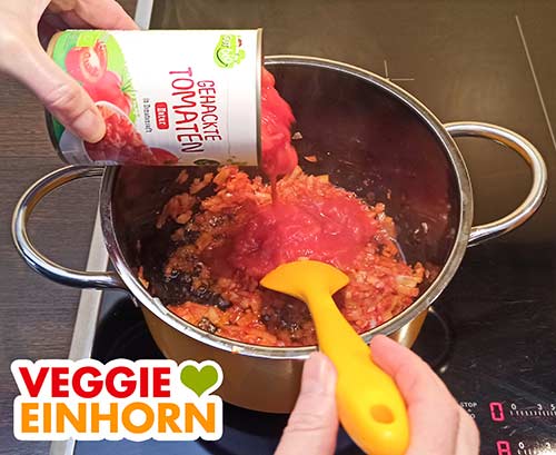 Eine 400 g Dose gehackte Tomaten zufügen. Eine Dose Tomatenstücke wird in den Topf zugefügt.