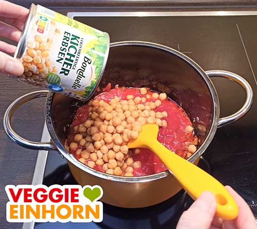 Kichererbsen und Flüssigkeit aus der Dose zufügen. Eine Dose Kichererbsen wird in den Topf zugefügt.