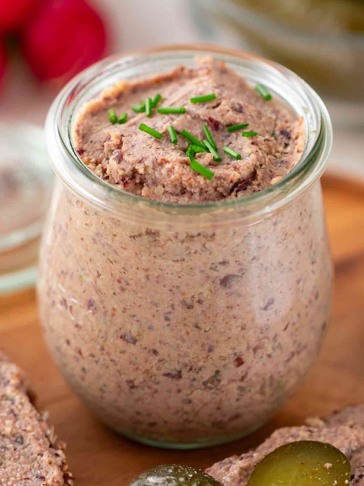 Nahaufnahme von einem Glas mit veganer Leberwurst, garniert mit frischem Schnittlauch.