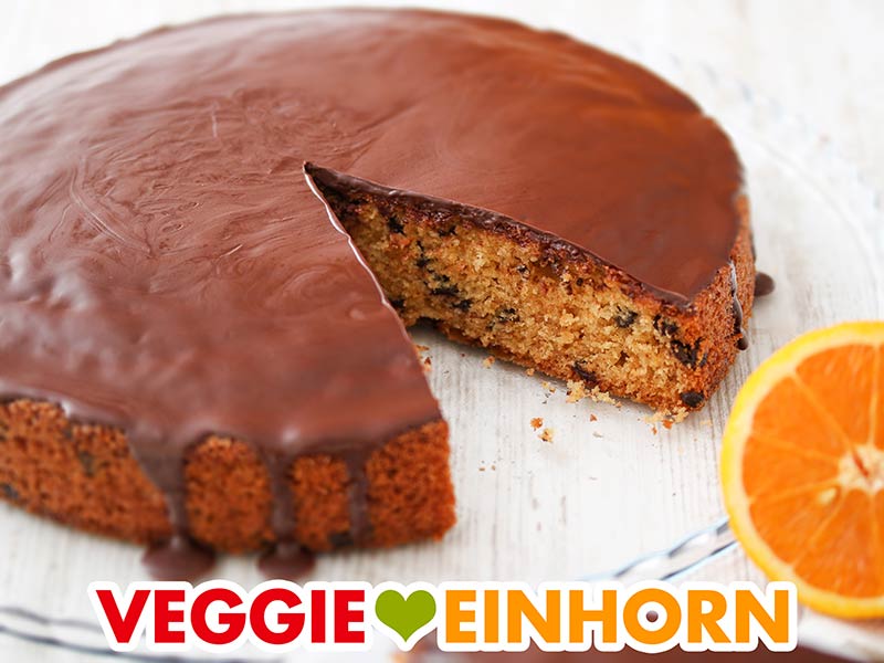 Veganer Orangenkuchen mit Schokolade Ein angeschnittener Orangenkuchen auf einer Kuchenplatte