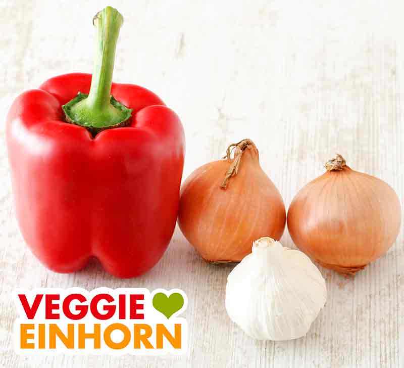 Paprika, Zwiebeln und Knoblauch für vegetarisches Gulasch Eine rote Paprika, zwei Zwiebeln und eine Knoblauchknolle