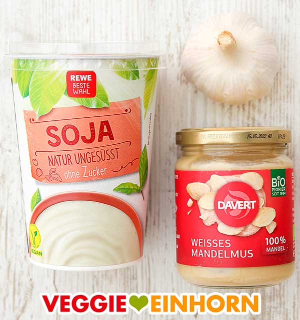Ungesüßter Pflanzenjoghurt, frischer Knoblauch und Nussmus Ein Becher Sojajoghurt, eine Knoblauch Knolle, ein Glas weißes Mandelmus