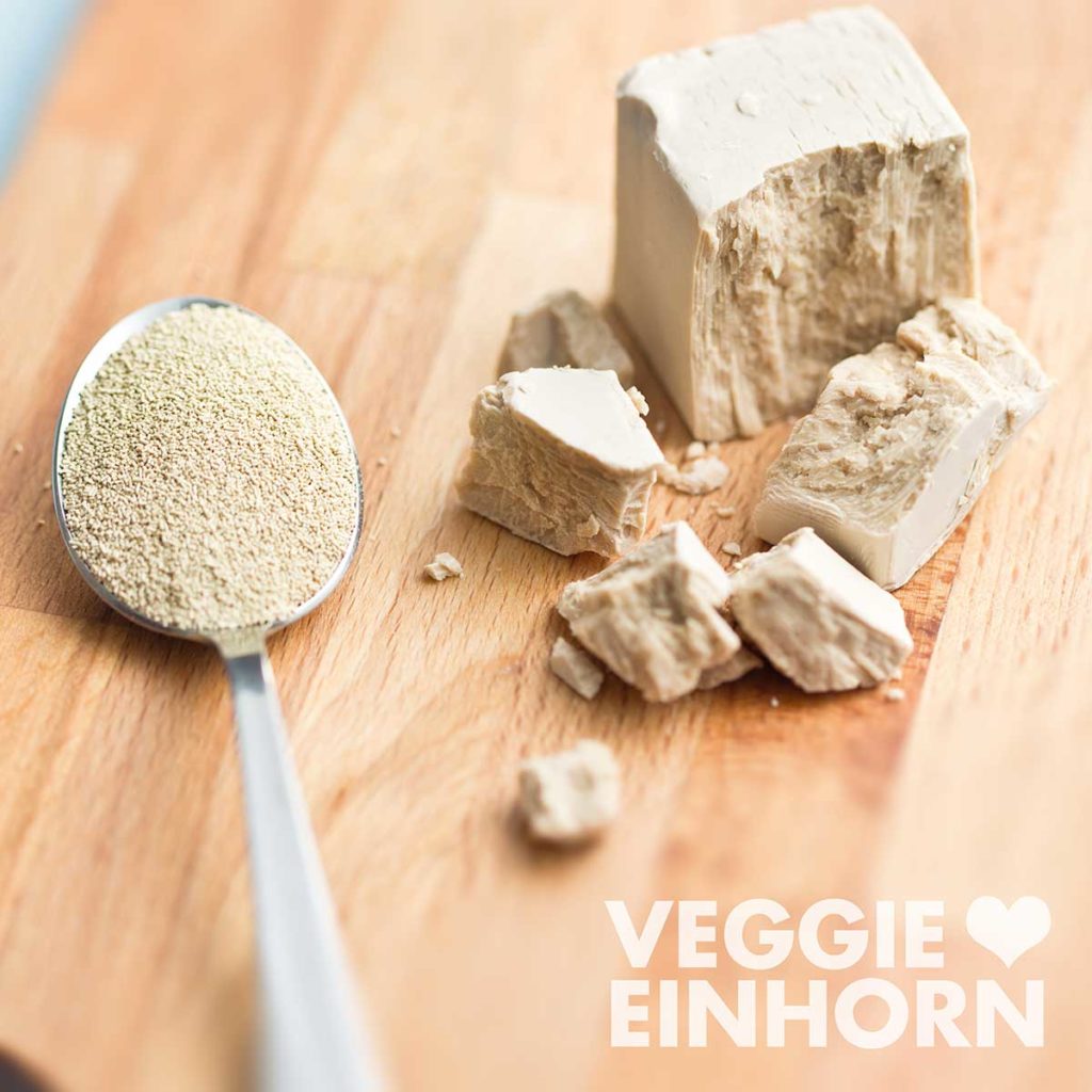 Ein Teelöffel mit Trockenhefe und ein Würfel frische Hefe