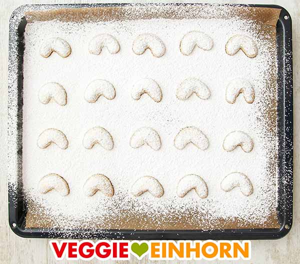 Vanillekipferl mit Puderzucker auf dem Backblech Die veganen Vanillekipferl kühlen auf dem Backblech ab.