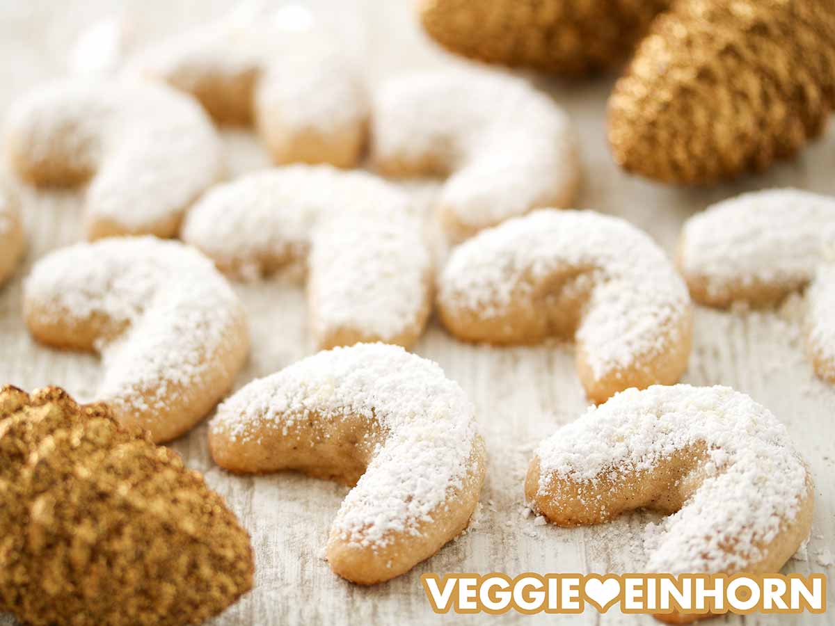 Mit Puderzucker bestreute Vanillekipferl und goldene Tannenzapfen auf einem Tisch