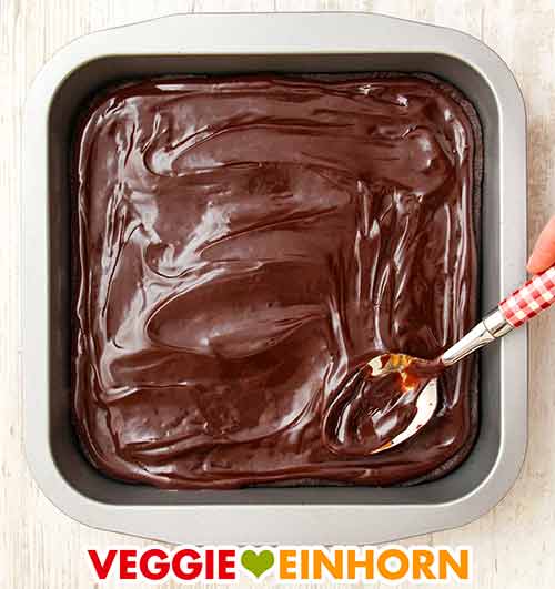 Der Schokoüberzug wird mit einem Esslöffel auf den Brownies verteilt. Verteilen des Schokoladenüberzuges auf den Brownies mit einem Esslöffel