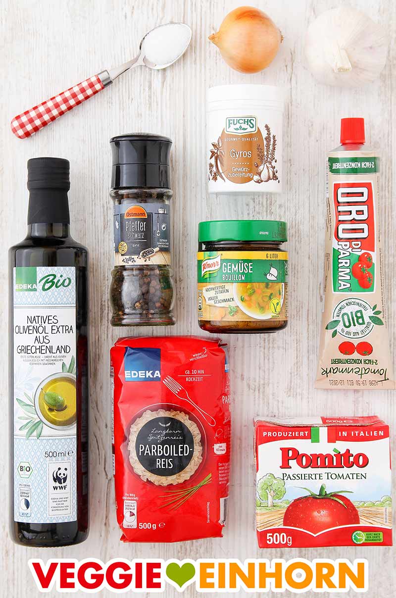 Zutaten für veganen Tomatenreis auf einem hellen Holzhintergrund: Olivenöl, schwarzer Pfeffer, Gyrosgewürz, Gemüsebrühe, Tomatenmark, passierte Tomaten, Parboiled-Reis, Zwiebel, Knoblauch und ein Löffel Zucker