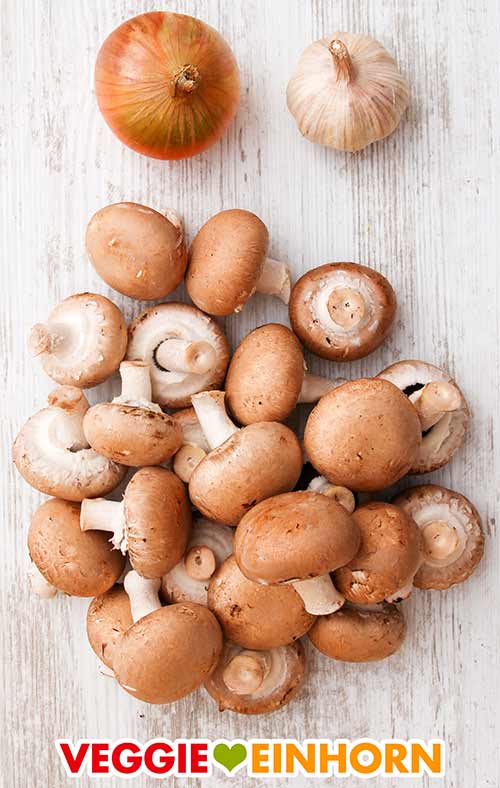 Zwiebel, Knoblauch und Pilze Eine Zwiebel, eine Knoblauchknolle und ein Haufen brauner Champignons