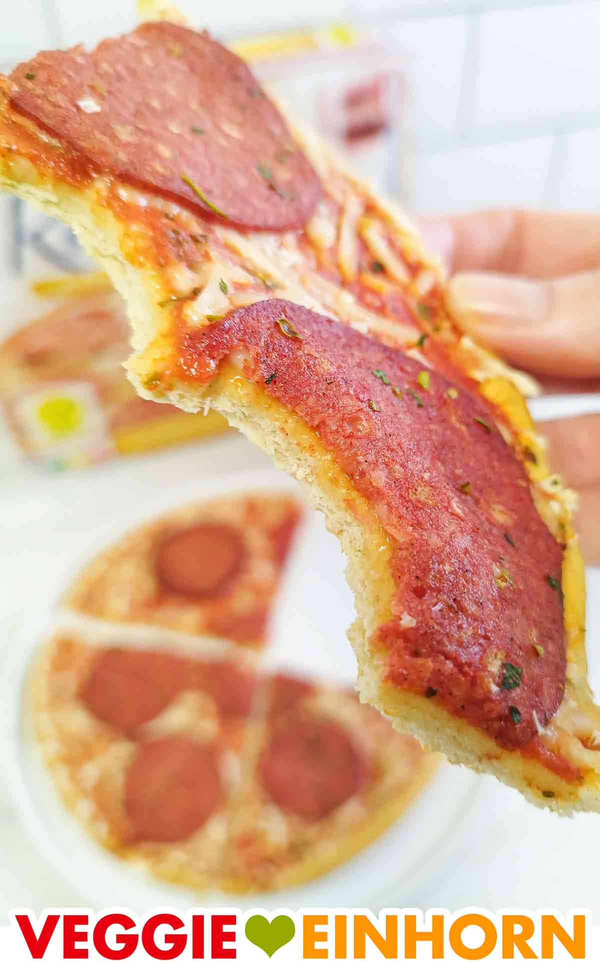 Hier sieht man den dünnen, knusprigen Boden. Angebissenes Pizzastück mit veganer Salami von Dr. Oetker