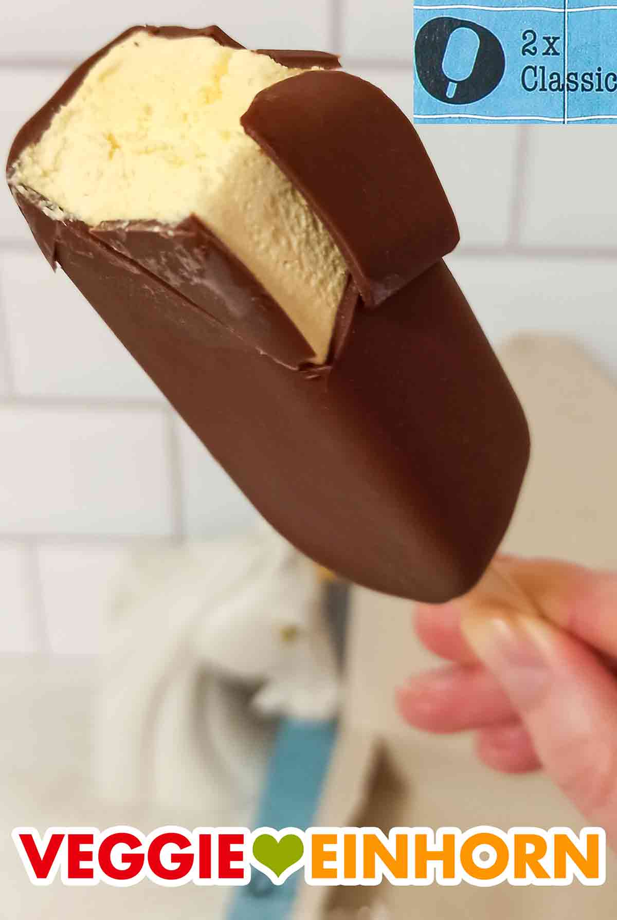 Das Stieleis Classic von Food For Future hat knackige vegane Schokolade und cremige vegane Vanilleeiscreme. Angebissenes veganes Stieleis in der Sorte Classic