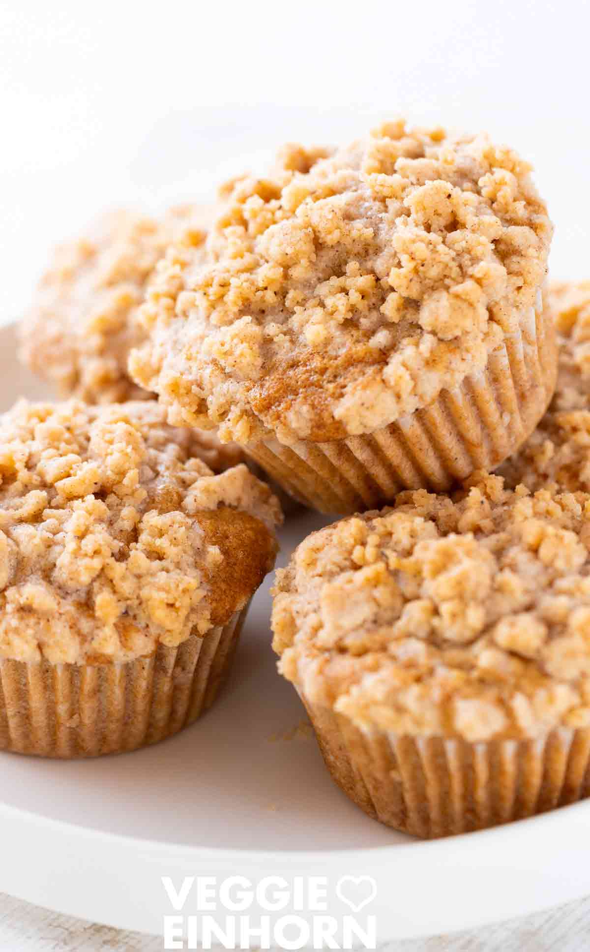 Nahaufnahme von veganen Apfel-Streusel-Muffins auf einem weißen Teller.