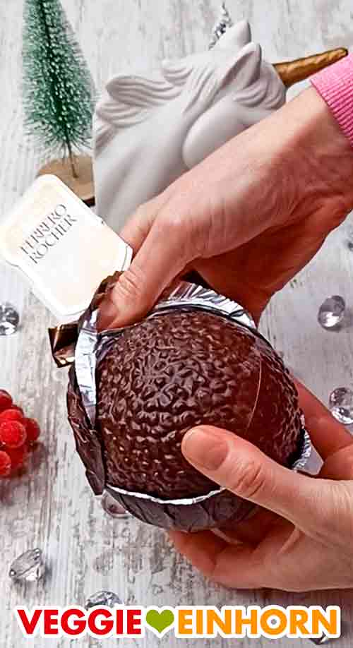 Auspacken der Schokoladenkugel des veganen Grand Ferrero Rocher Die Alufolie wird von der Schokokugel abgezogen.