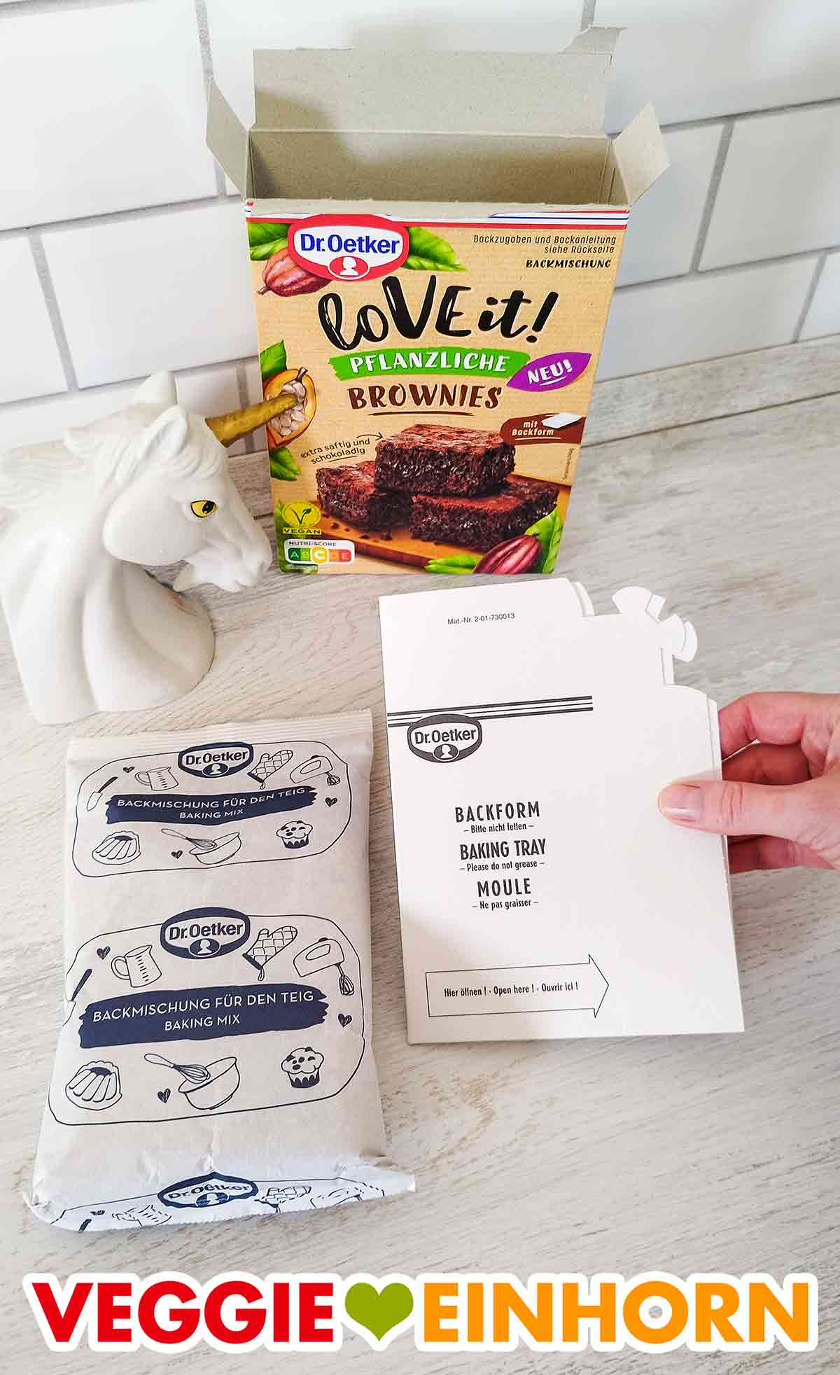 Die Packung enthält eine Tüte mit veganer Brownie Backmischung und eine Backform zum selber falten. Beutel mit Backmischung und Brownie Backform aus Pappe