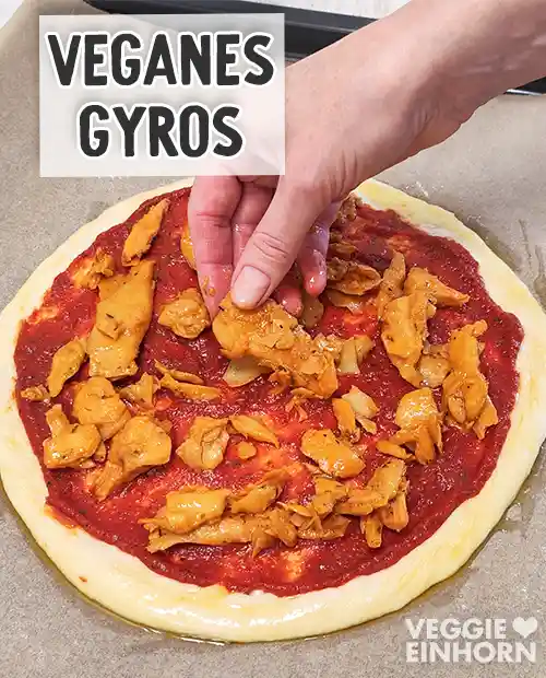 Ein runder Pizzaboden mit Tomatensauce wird mit Stücken von veganem Gyros belegt.