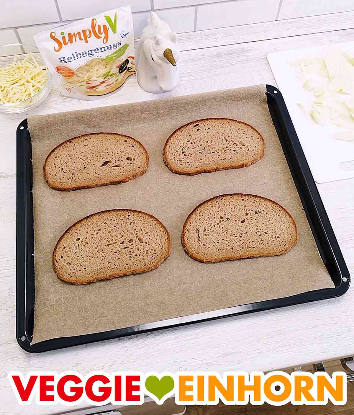 Vier Mischbrot Scheiben auf einem mit Backpapier ausgelegten Backblech. Backblech mit Backpapier und vier Scheiben Graubrot.
