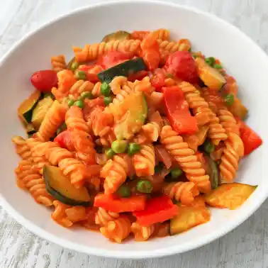 Teller mit cremiger veganer One Pot Pasta mit Zucchini, Paprika und Erbsen.