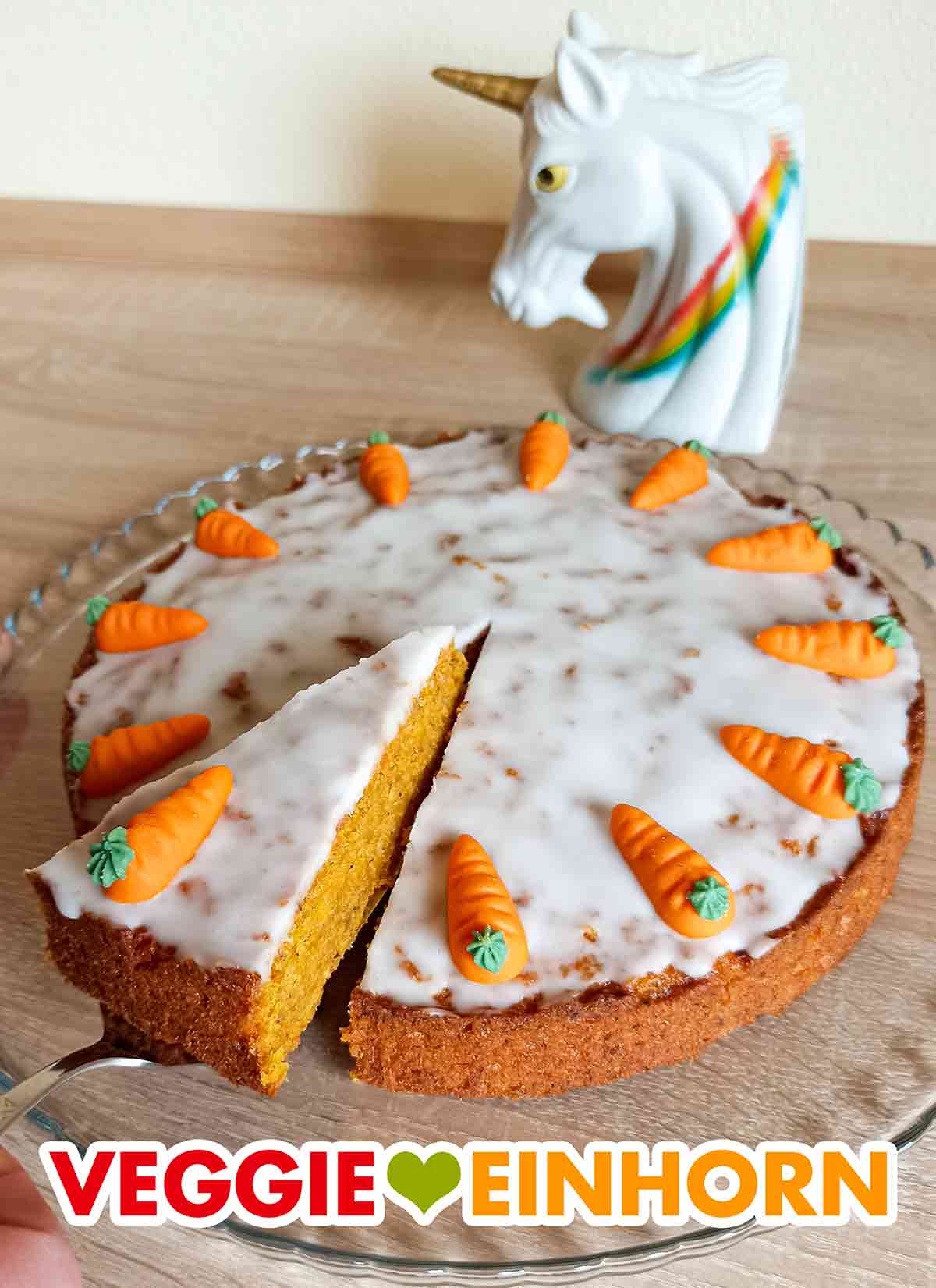 Der vegane Karottenkuchen wird serviert. Ein Stück des angeschnittenen Karottenkuchens wird entnommen.