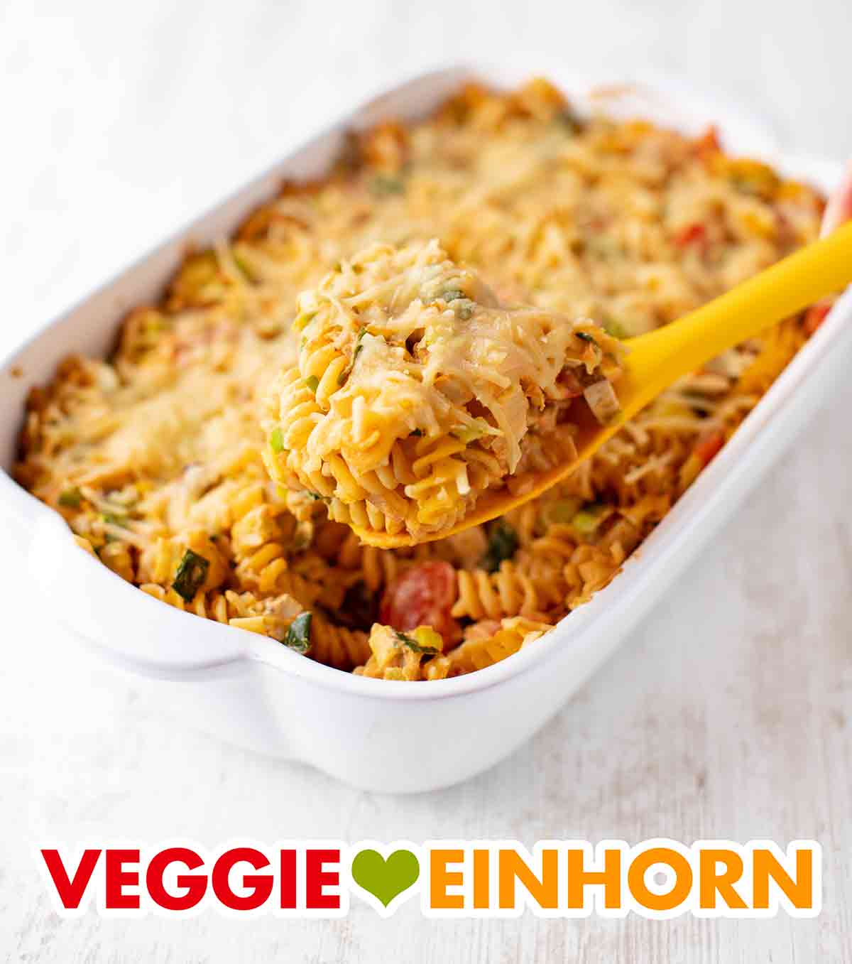 Der vegane Nudelauflauf mit Räuchertofu, Lauch und Tomaten wird serviert. Servierlöffel mit veganem Nudelauflauf mit Räuchertofu, Lauch und Tomaten