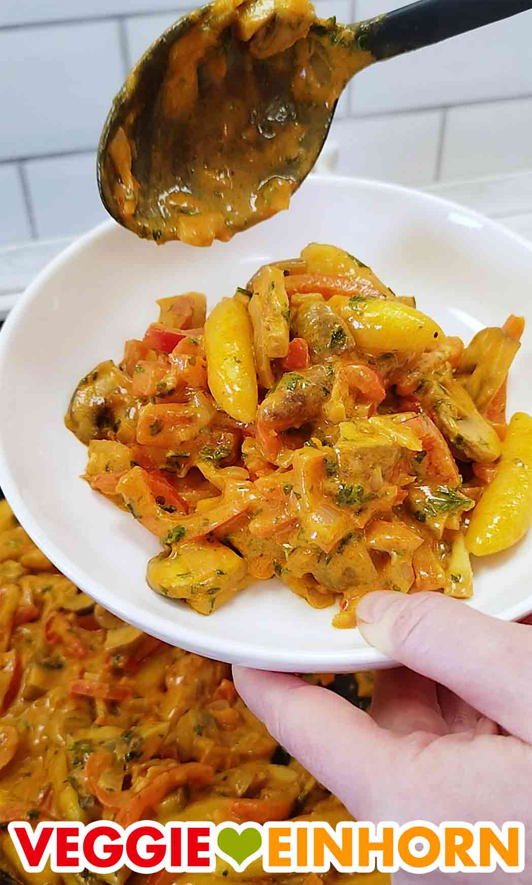 Die vegane Schupfnudel Pfanne wird auf einen Teller gefüllt. Auffüllen der veganen Schupfnudelpfanne auf einen Teller mit einem Servierlöffel