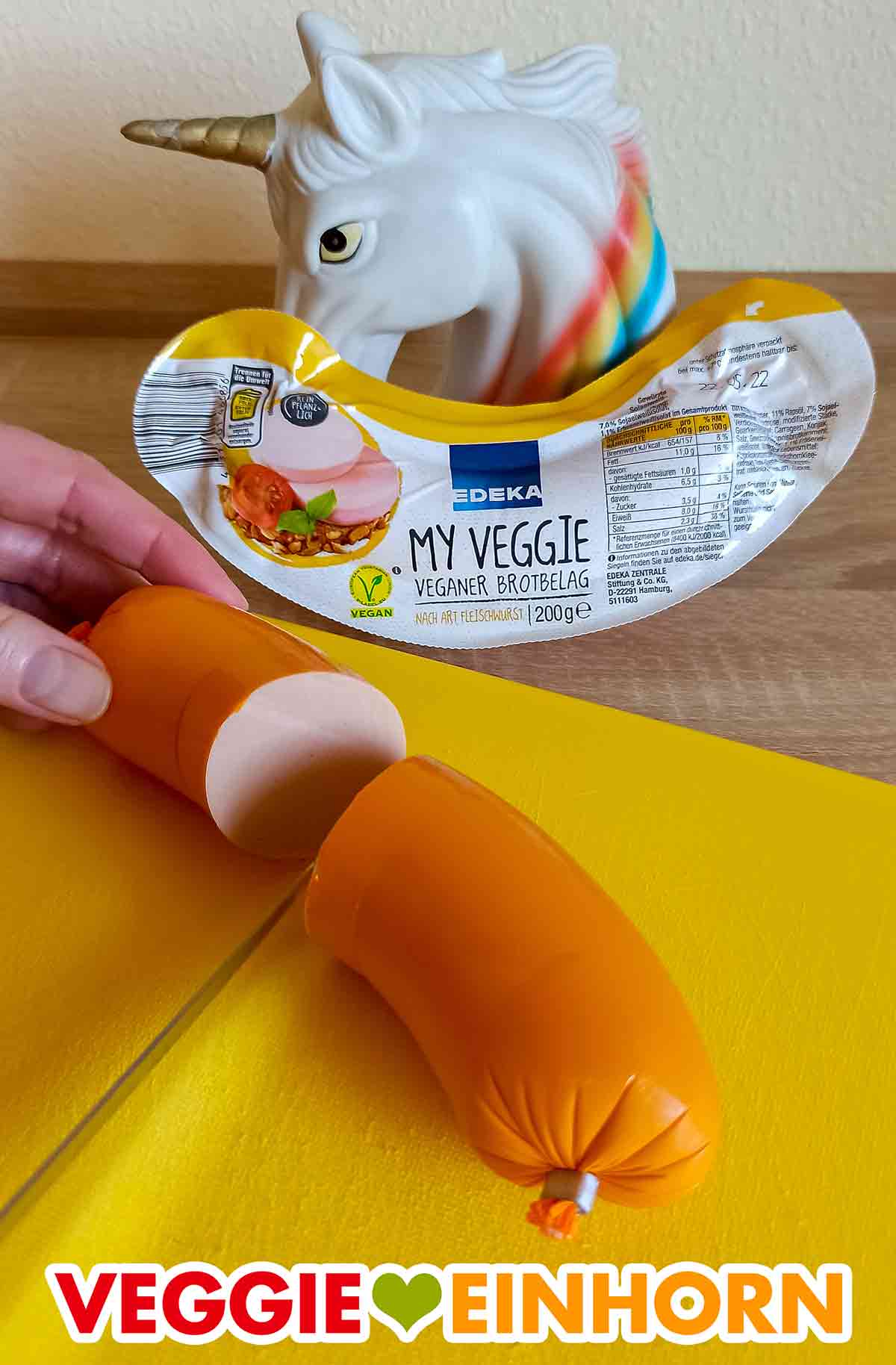Die Fleischwurst My Veggie Veganer Brotbelag auf einem Schneidebrett Die vegane Fleischwurst von Edeka wird mit einem Messer durchgeschnitten.