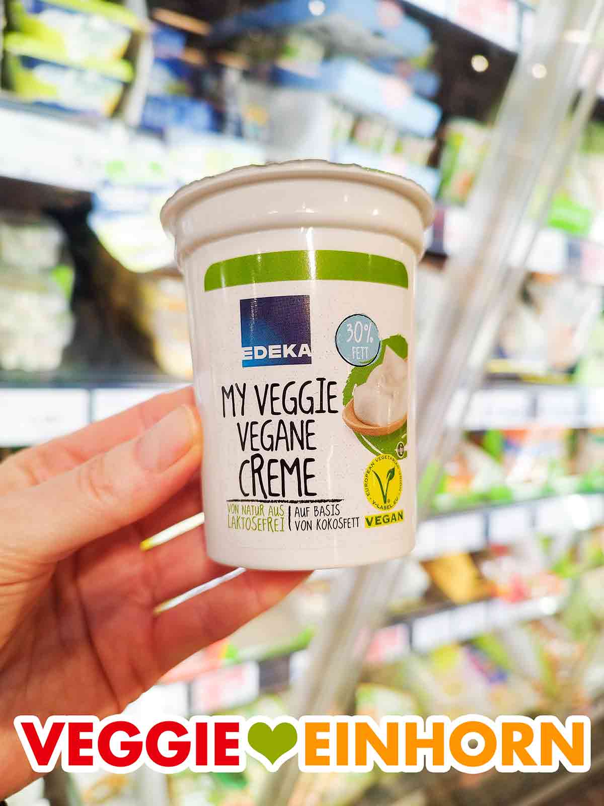 Die Vegane Crème fraîche von Edeka ist auf Basis von Kokosfett und Sojaeiweiß. Eine Hand hält einen Becher Vegane Creme von Edeka