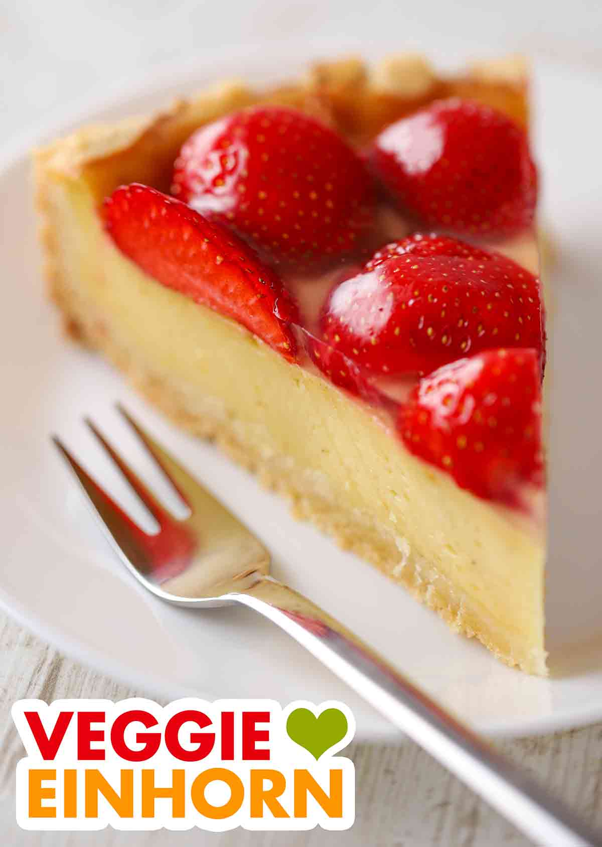 Der vegane Käsekuchen mit frischen Erdbeeren ist ein beliebter veganer Kuchen. Ein Stück veganer Käsekuchen mit Erdbeeren auf einem Kuchenteller