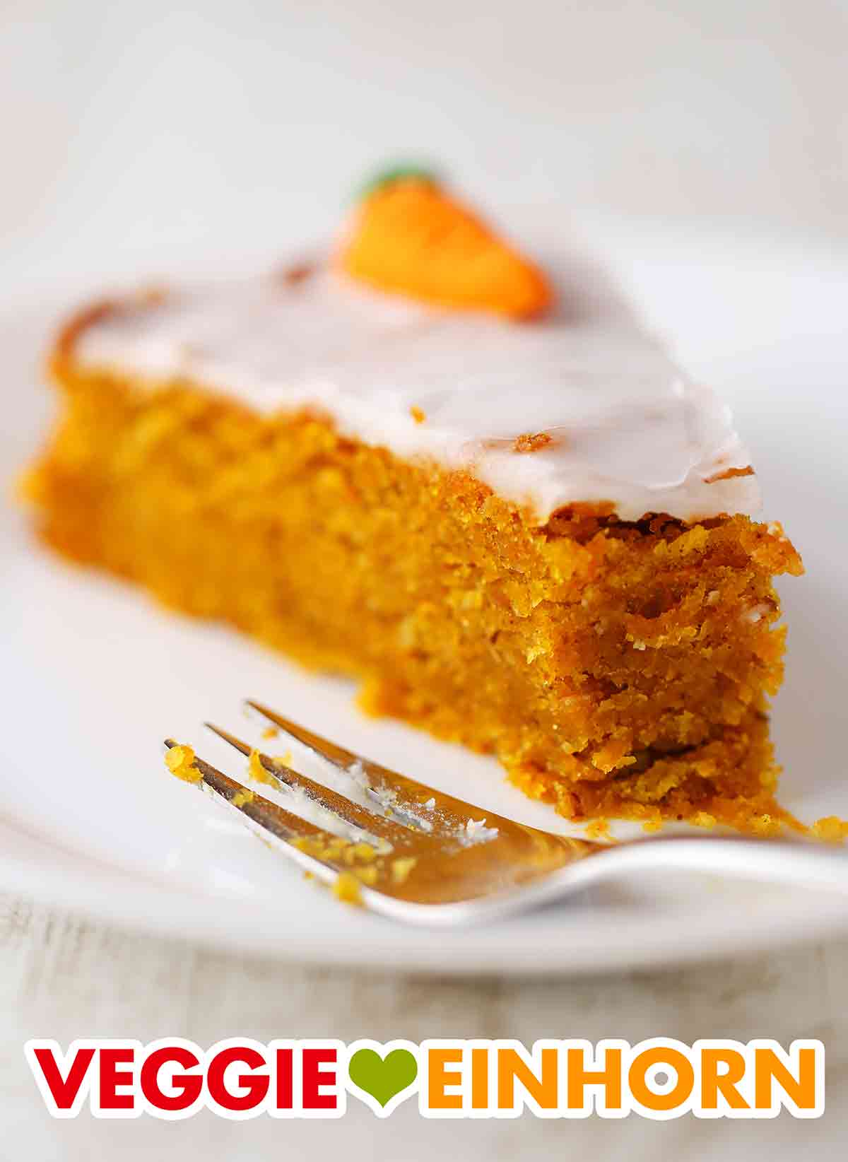 Der vegane Karottenkuchen mit Haselnüssen und Apfelmus auf einem Kuchenteller mit einer Kuchengabel. Ein Stück veganer Karottenkuchen auf einem Kuchenteller