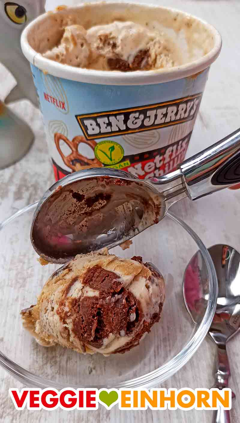 Hier sieht man die leckeren Brownie Stückchen auf der Eiskugel. Eine Kugel veganes Netflix and Chill'd Eis wird mit einem Eisportionierer in ein Glasschälchen gegeben.