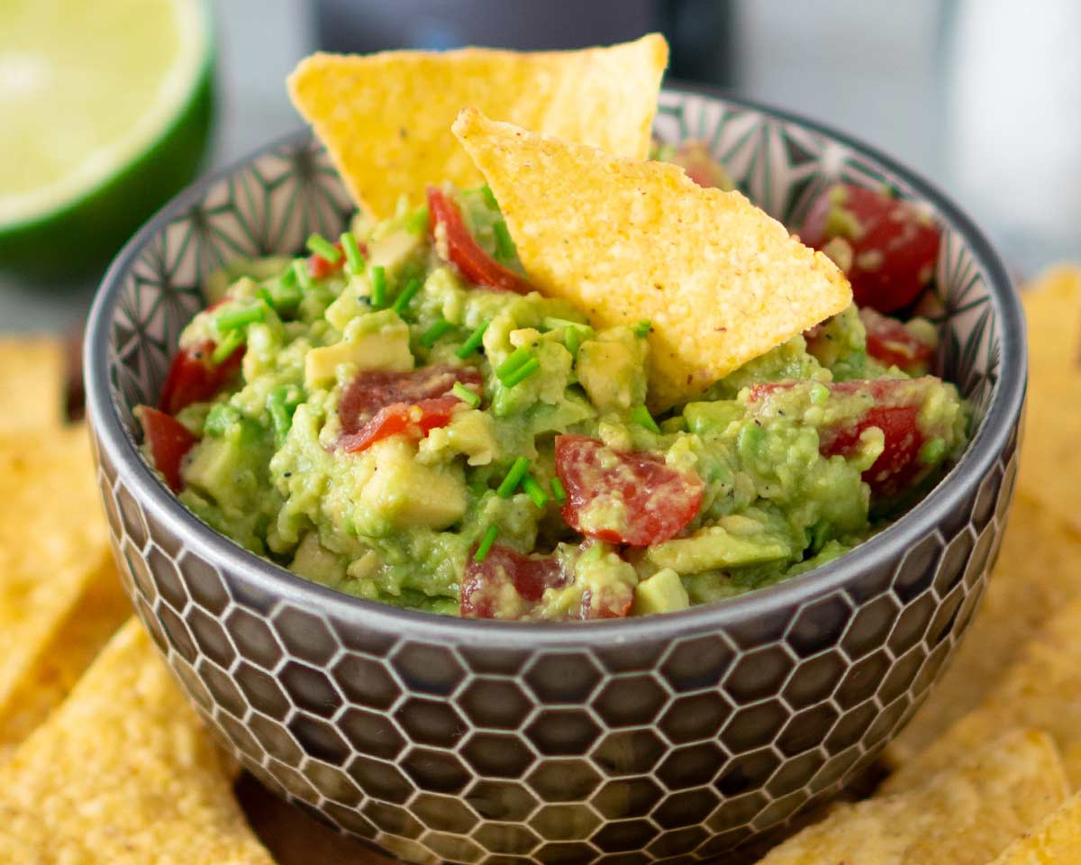 Schüssel mit Guacamole mit Tomaten, garniert mit Schnittlauch und serviert mit Tortilla-Chips