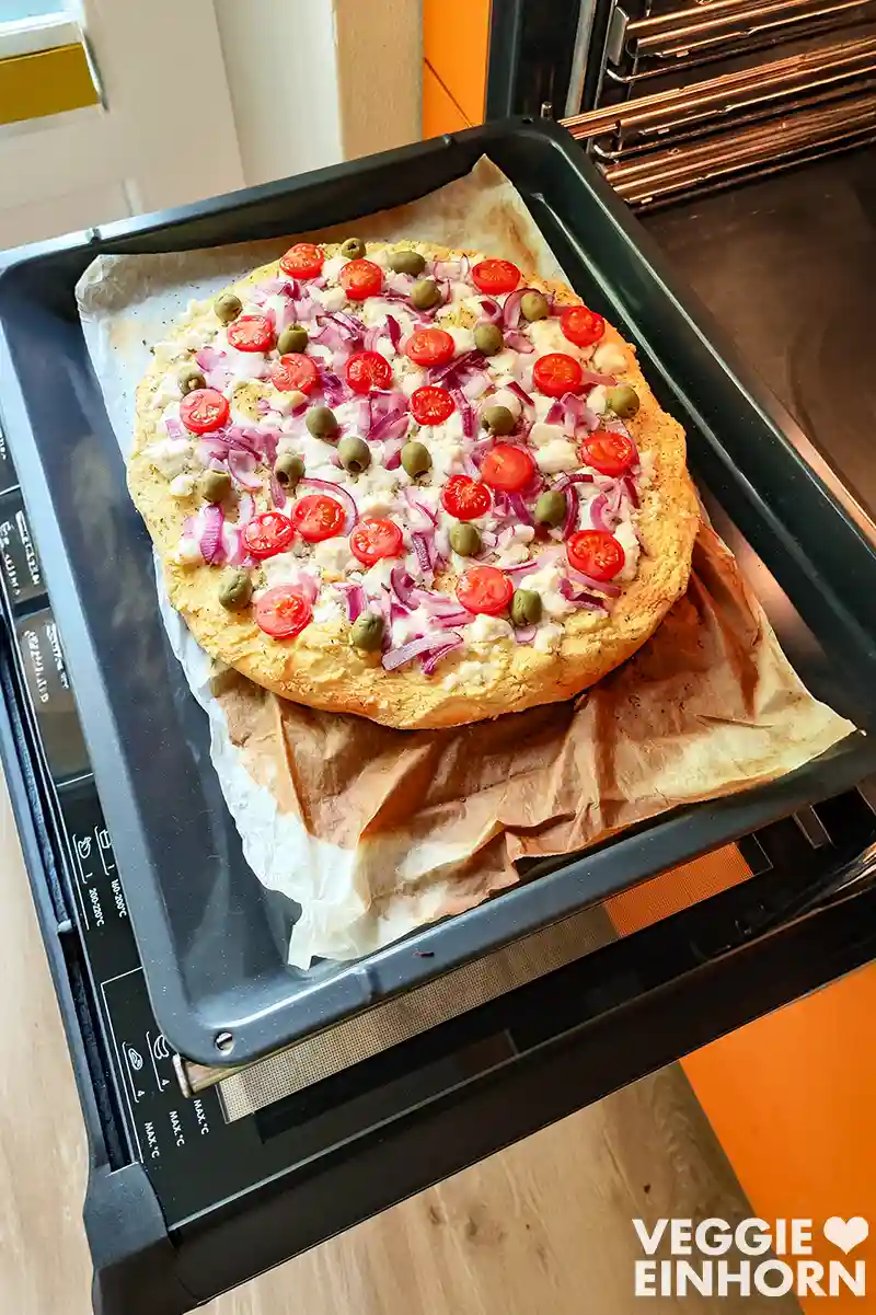 Vegane Hummus-Pizza auf dem Backblech im geöffneten Ofen.
