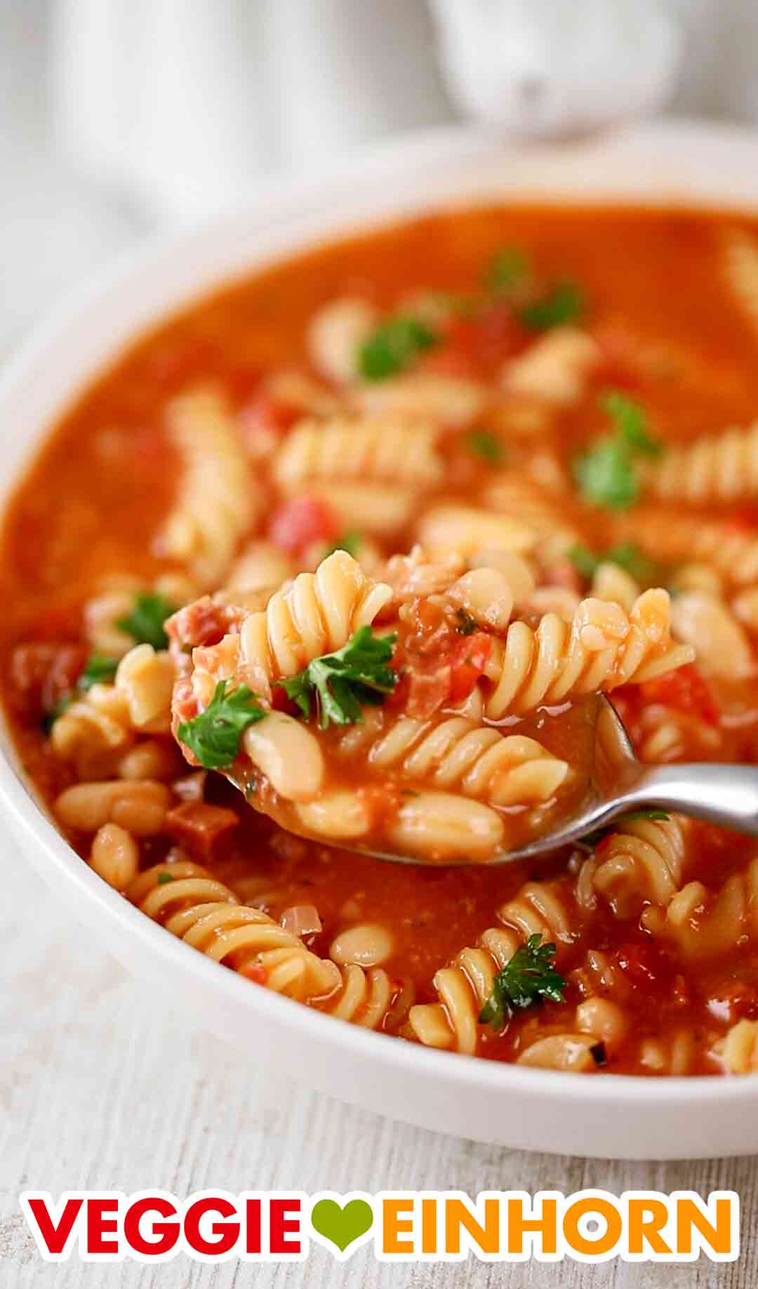 Italienische weiße Bohnensuppe mit veganem Speck und Nudeln Italienische Nudelsuppe mit weißen Dosenbohnen und veganem Speck auf einem Esslöffel