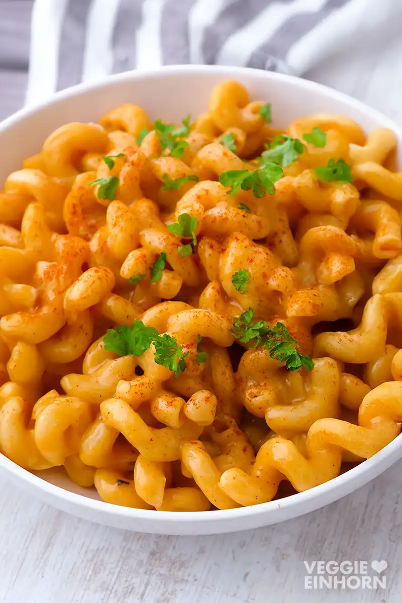 Ein Teller mit veganen Macaroni and Cheese mit einer veganen Käsesoße mit veganem Cheddar. Die Nudeln sind mit Petersilie und Paprikapulver garniert.