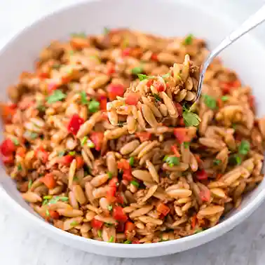 Weiße Schüssel mit Kritharaki Salat aus Nudeln, veganem Hackfleisch, roten Paprikastücken und frischen Kräutern, eine Gabel hält etwas von dem Salat über der Schüssel.