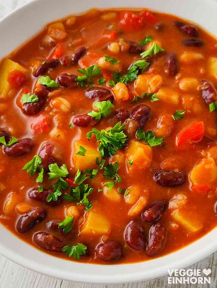 Veganer Bohneneintopf mit Kartoffeln und Petersilie auf einem weißen Teller.
