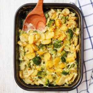 Veganer Kartoffel-Brokkoli-Auflauf in einer schwarzen Form, ein Holzlöffel liegt darin.