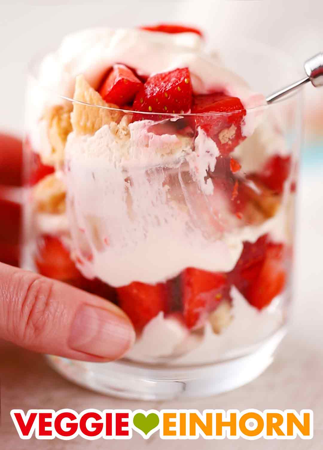 Das vegane Erdbeerdessert wird aus dem Glas gelöffelt. Löffel in Glas mit veganem Erdbeernachtisch