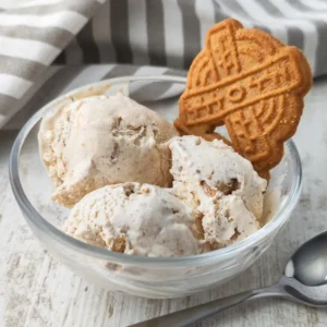 Veganes Spekulatius Eis in einer Glasschale mit einem Spekulatiuskeks und einem Löffel auf hellem Holztisch serviert.