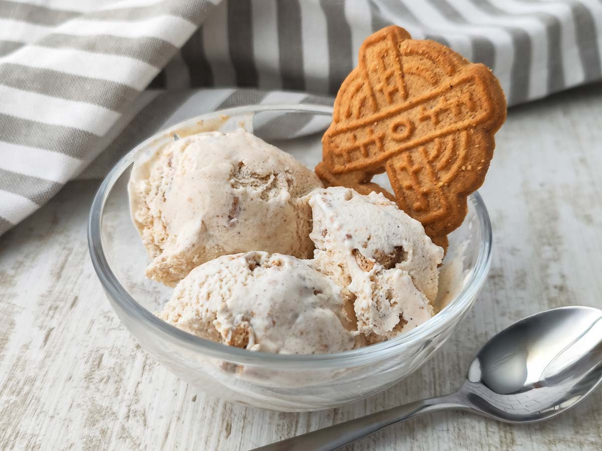 Drei Kugeln cremiges veganes Spekulatius Eis mit kleinen Keksstückchen in einer Glasschale auf hellem Untergrund.
