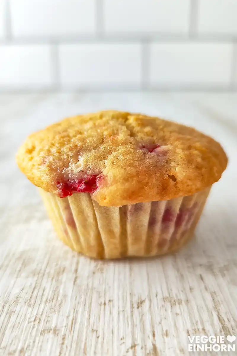 Veganer Erdbeermuffin in einem Papierförmchen auf weißem Holztisch.